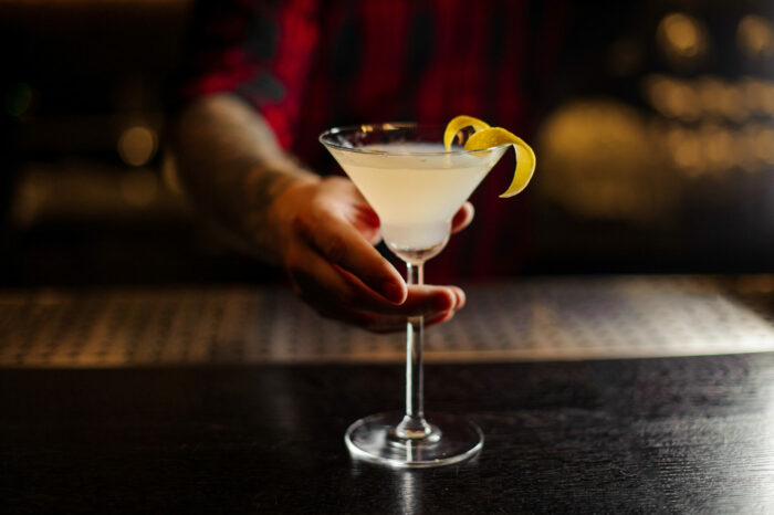 bartender serving a white lady cocktail decorated with orange zest