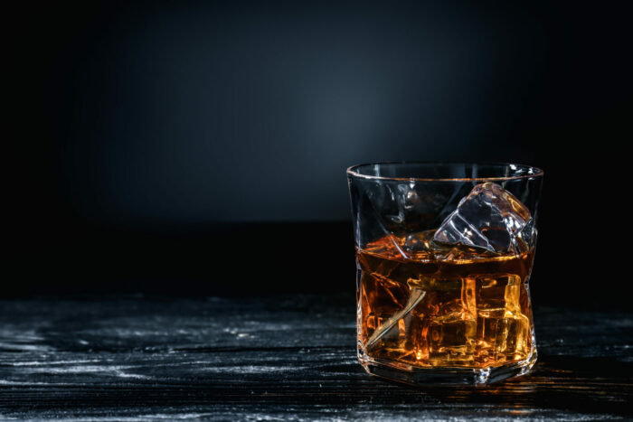 glass of whisky with ice on wooden table against dark background