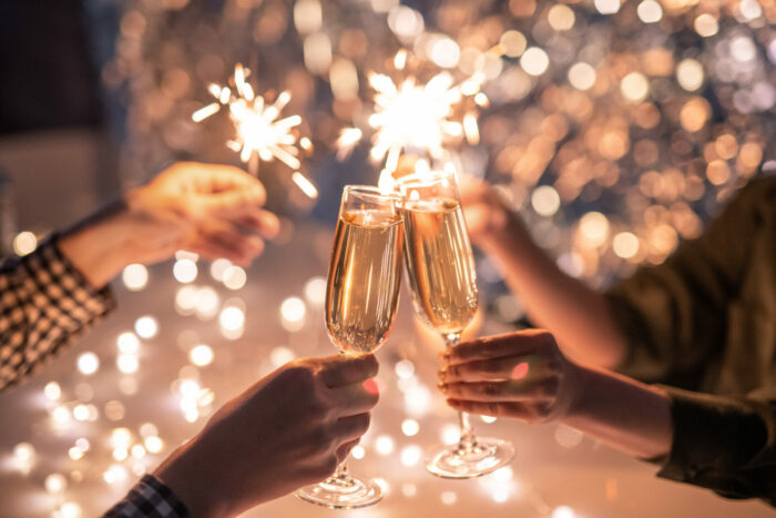 hands of couple with flutes of champagne and their friends with bengal lights